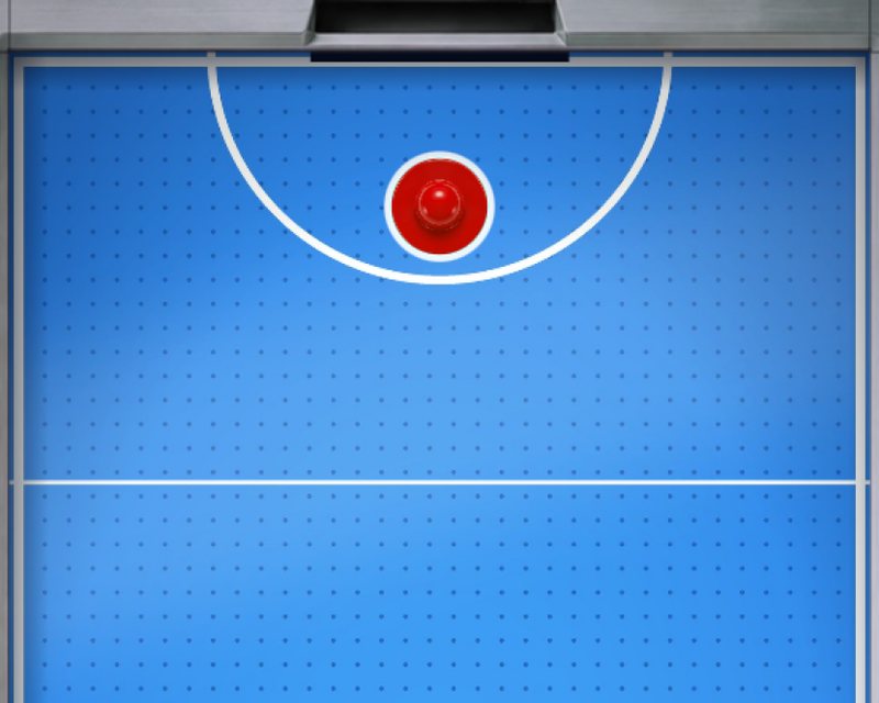 Looking down on an air hockey table, the red mallet waiting in its crease